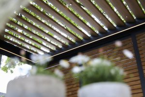 Les lames couleur bois de cette élégante pergola se mêlent harmonieusement à la verdure environnante, offrant une scè...