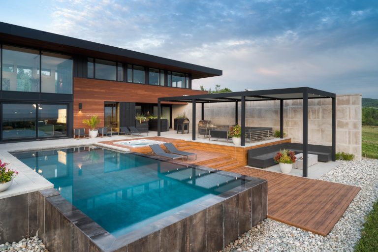 La photo illustre une élégante maison contemporaine dont l'architecture met en valeur une spectaculaire pergola bioclima...